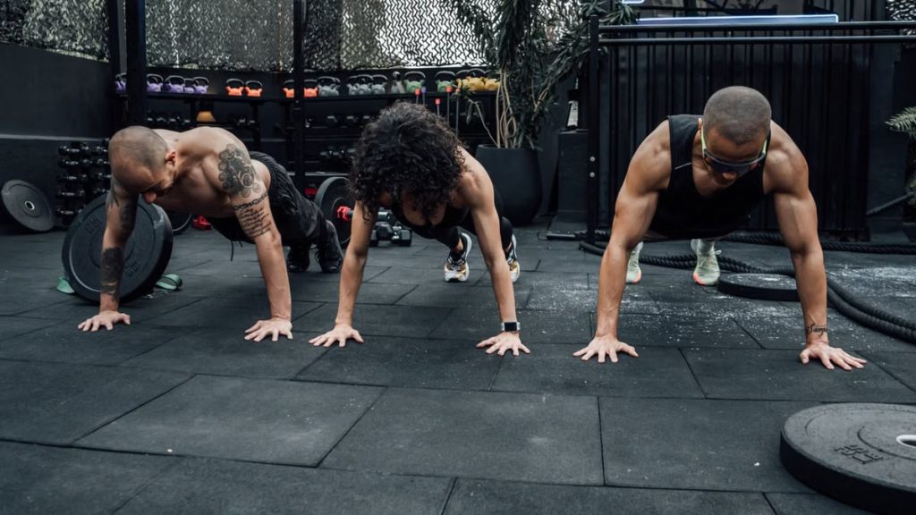 Three individuals performing push-ups together in a Mexico City gym setting.